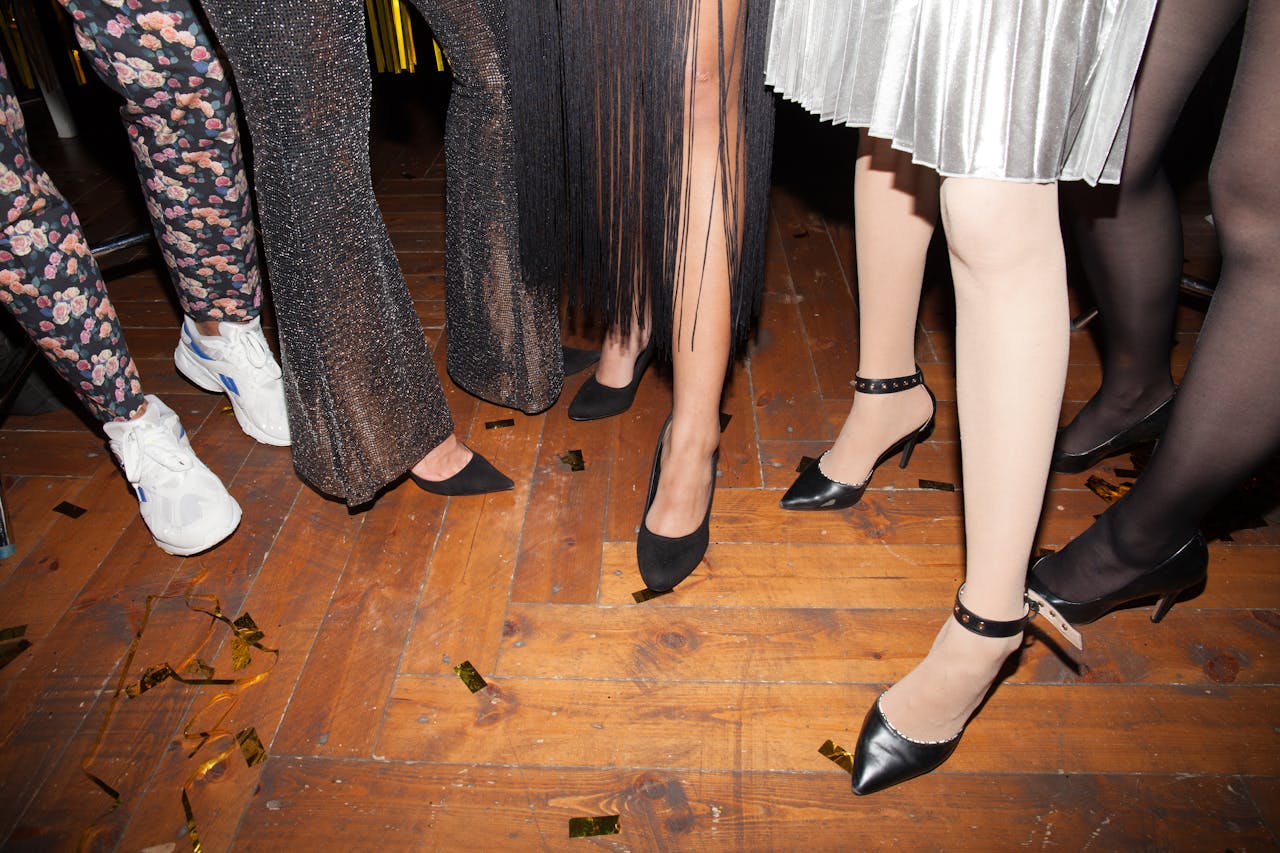 Womens legs in stylish outfits and footwear at a lively indoor party.